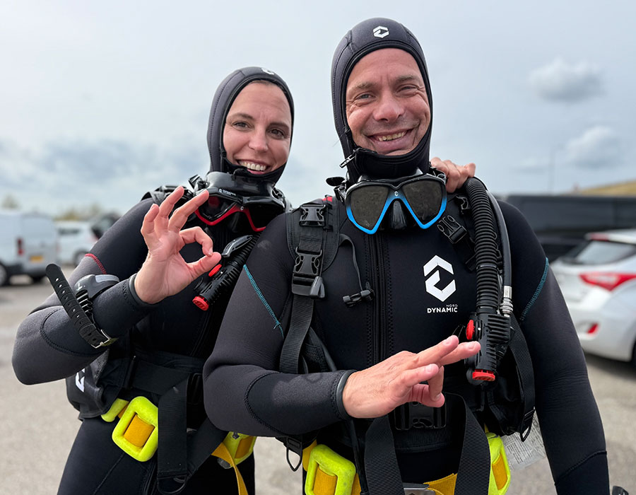 Lachende OWD-cursisten met duikuitrusting op de kant